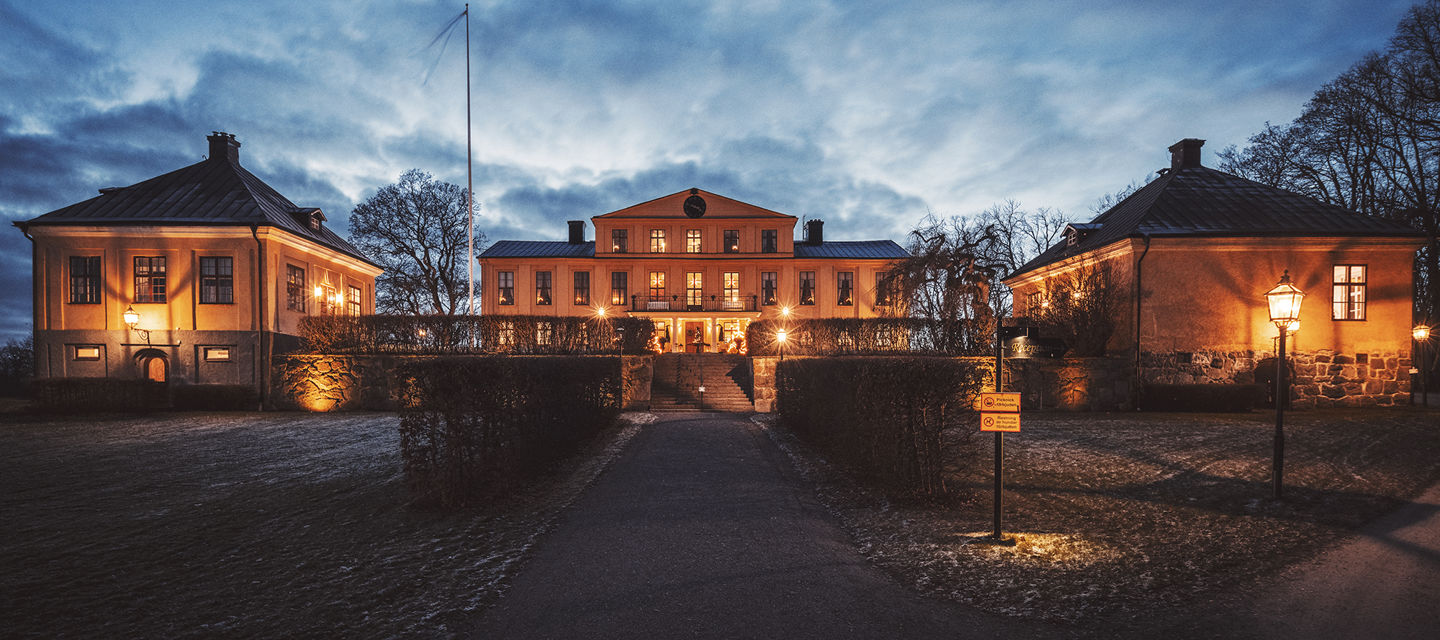 Herrgårdens fasad upplyst av lampor en höstkväll
